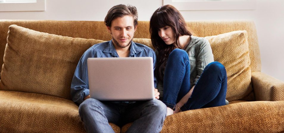 A man and woman sit comfortably on a couch looking at a computer, reading the latest news from WorldMark by Wyndham.