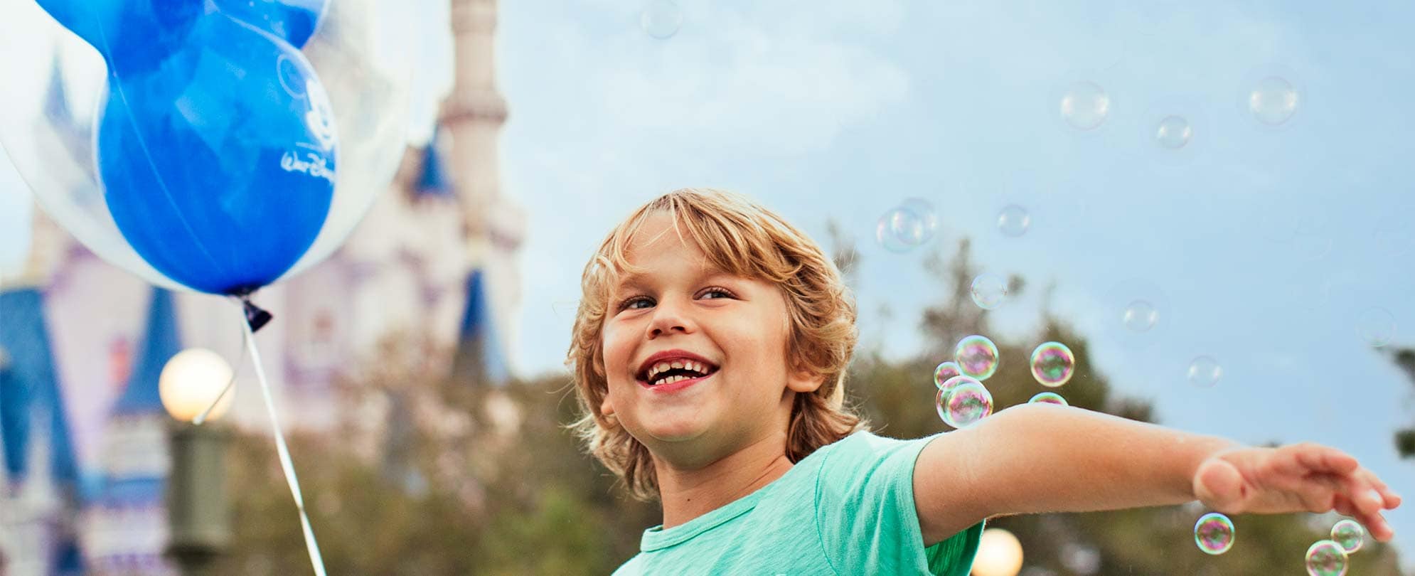 A smiling young boy surrounded by bubble holds a Mickey Mouse balloon at Disneyland in Anaheim, California.