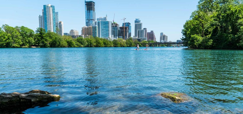 A lake surrounded by trees at Zilker Metropolitan Park with the Austin, Texas skyline in the distance.