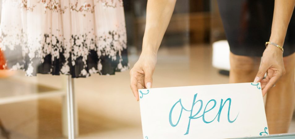 Two hands hold an "open" sign at boutique on Park Ave in Winter Park, Florida.