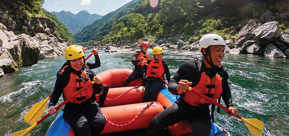 A group of people wearing life jackets and helmets smile while white water rafting.