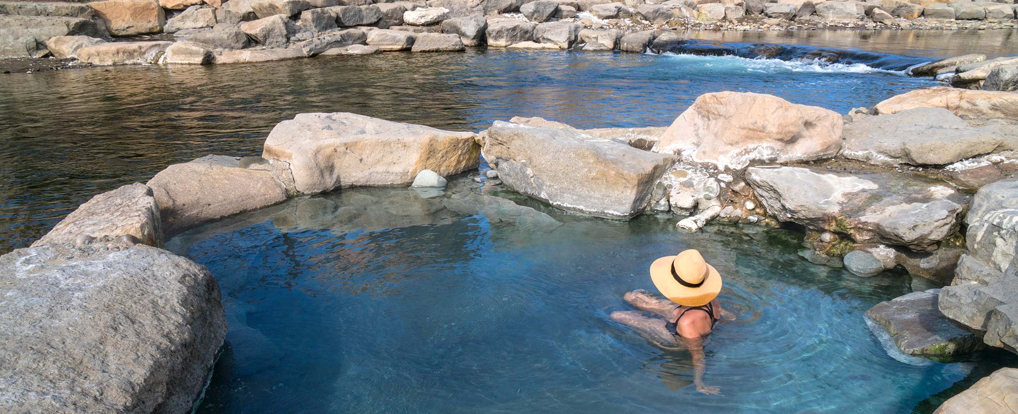 A woman wearing a sun hat sits in a pool of water surrounded by rocks at the San Juan River in Pagosa Springs, Colorado.