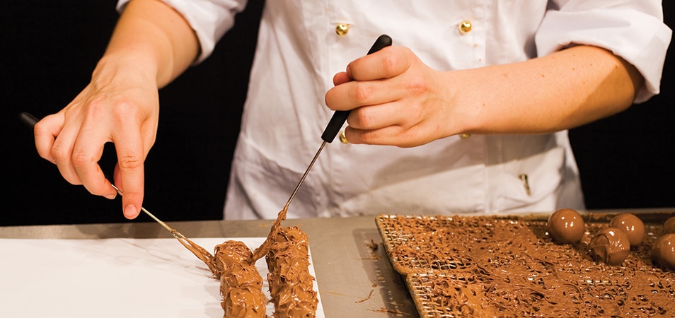 A chocolatier's hands as they prepare chocolate truffles.