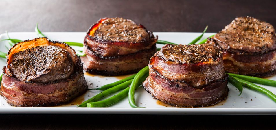 A plate of four bacon wrapped steak medallions with green beans at a restaurant in San Diego, California. 