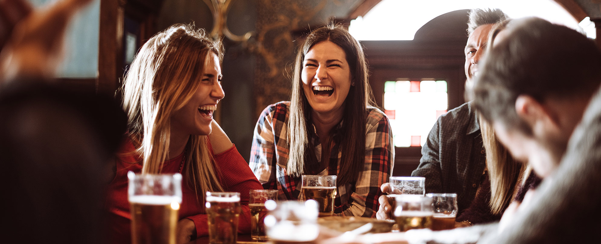 A group of friends are laughing while they drink beers, in a bar.