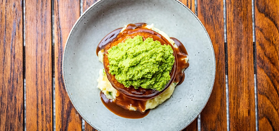 Australian pie with mashed potatoes, peas, and gravy sits on a plate.