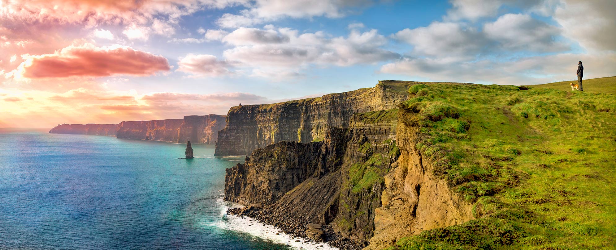 A man standing with his dog on the Cliffs of Moher in Ireland.