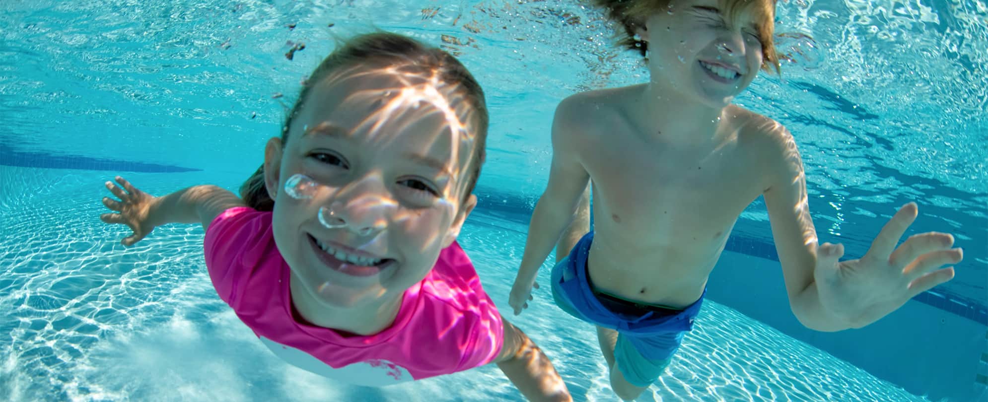 A little boy and girl, smiling underwater in a hotel pool.