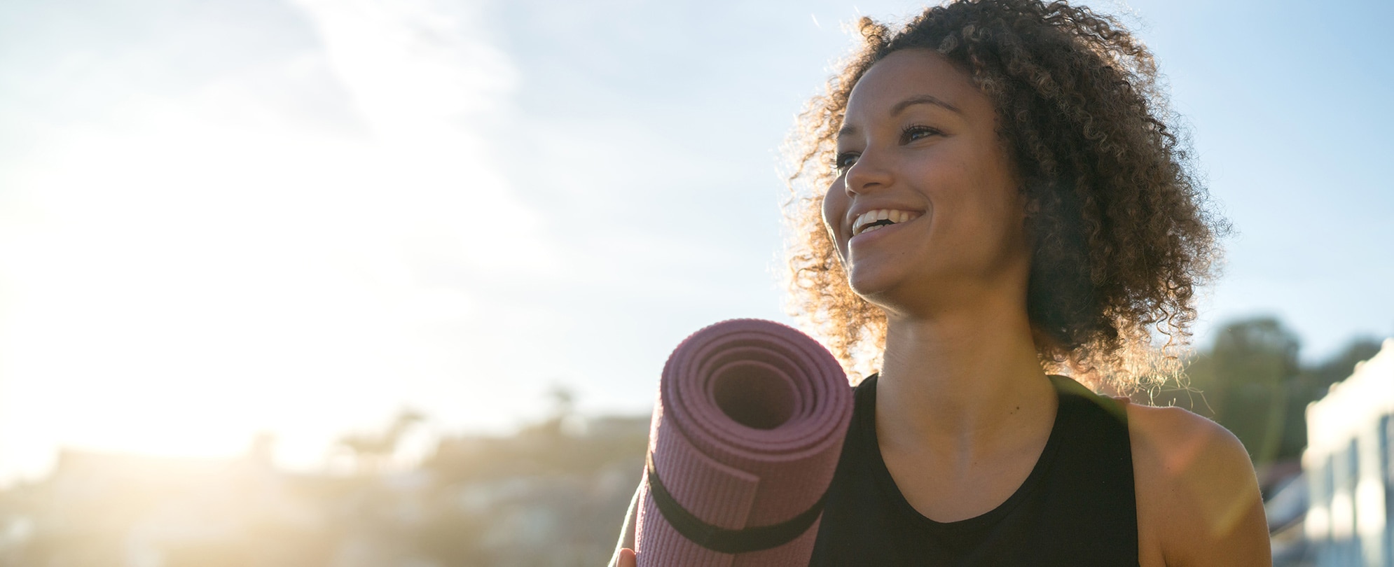 A smiling woman carrying a yoga mat