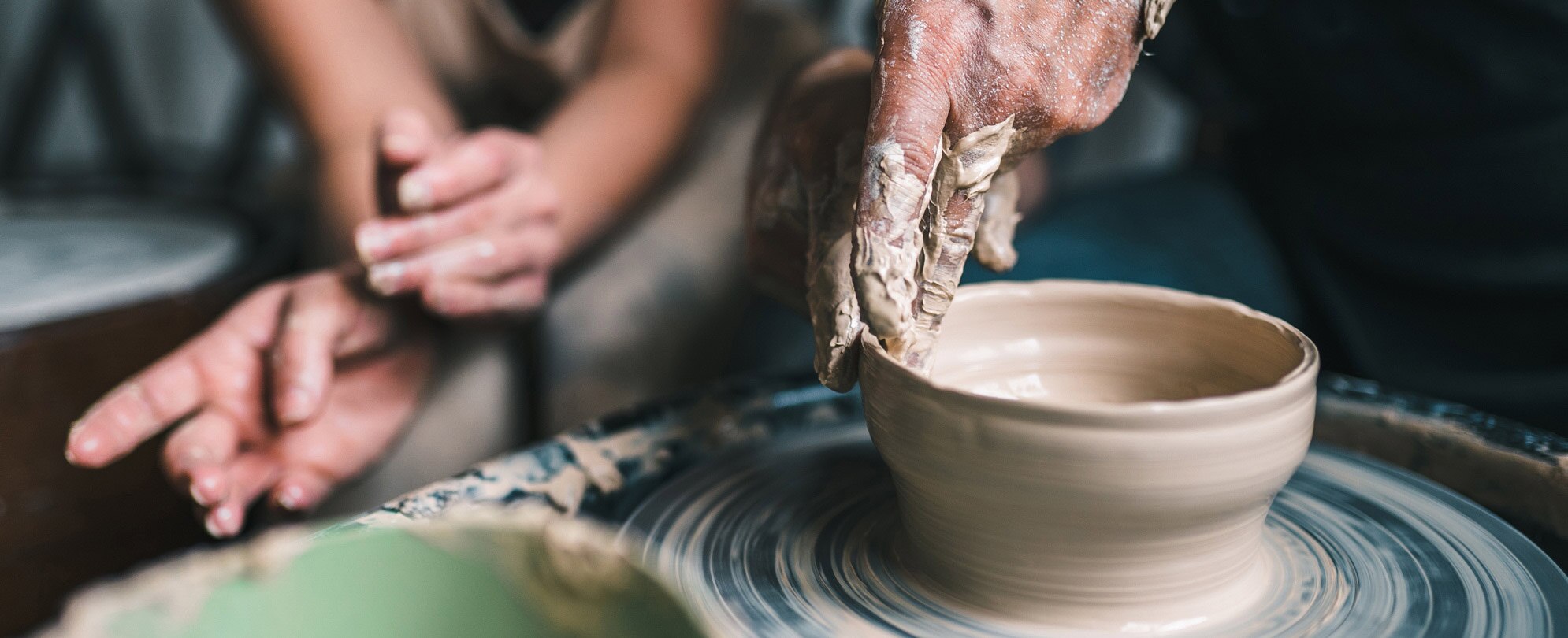 Hands forming a clay bowl on a pottery wheel