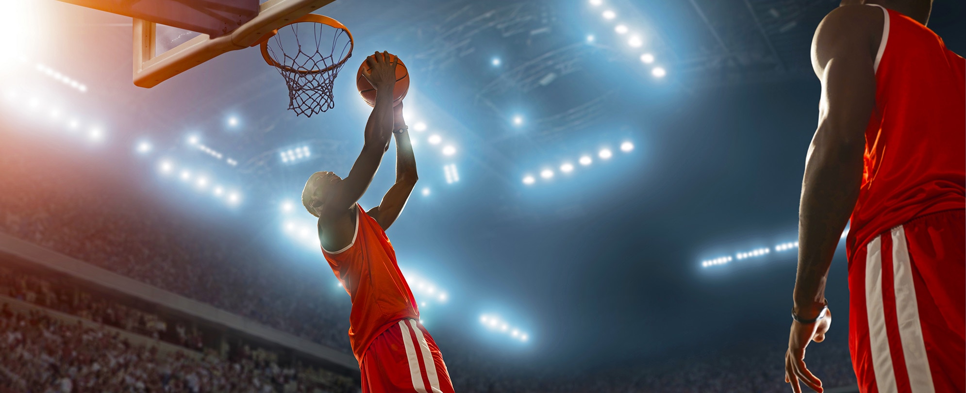 A basketball player holding a basketball and jumping for a reverse dunk at the net