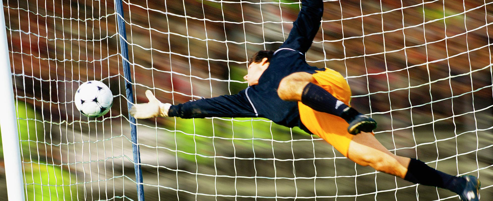 A soccer goalie jumping to reach a soccer ball flying into the net	