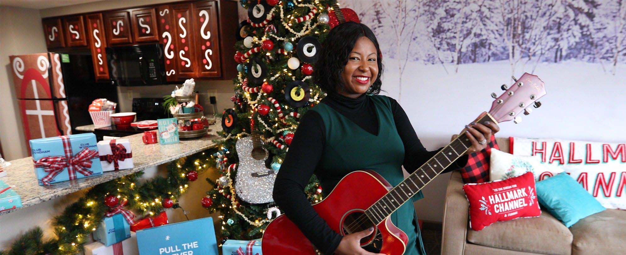 Melody poses with a guitar in front of a Christmas tree in the Hallmark Channel’s Countdown to Christmas Holiday Suite by Club Wyndham at Club Wyndham Nashville