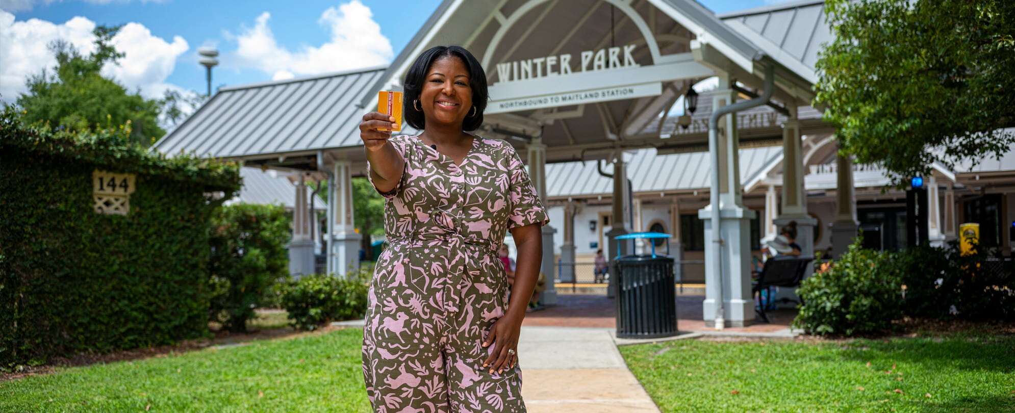 A woman is holding a travel ticket in front of a sign that says Winter Park.