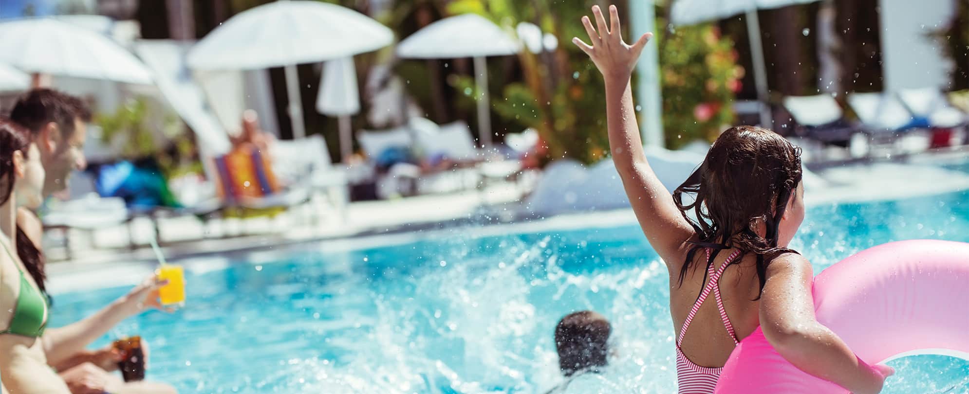 A girl holding a pink tube jumps into a pool at a Club Wyndham resort as her family watches