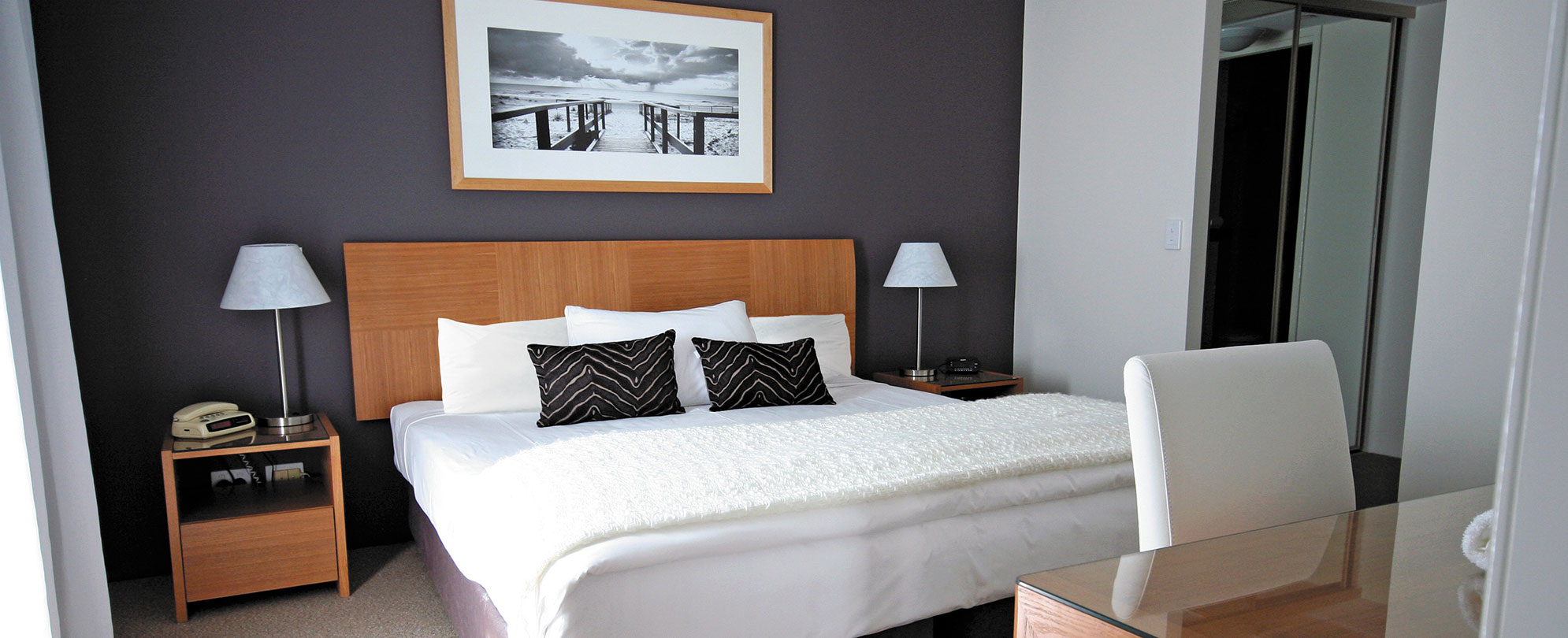 A bed, two side tables with lamps, and a desk in a Club Wyndham Crown Towers suite bedroom.