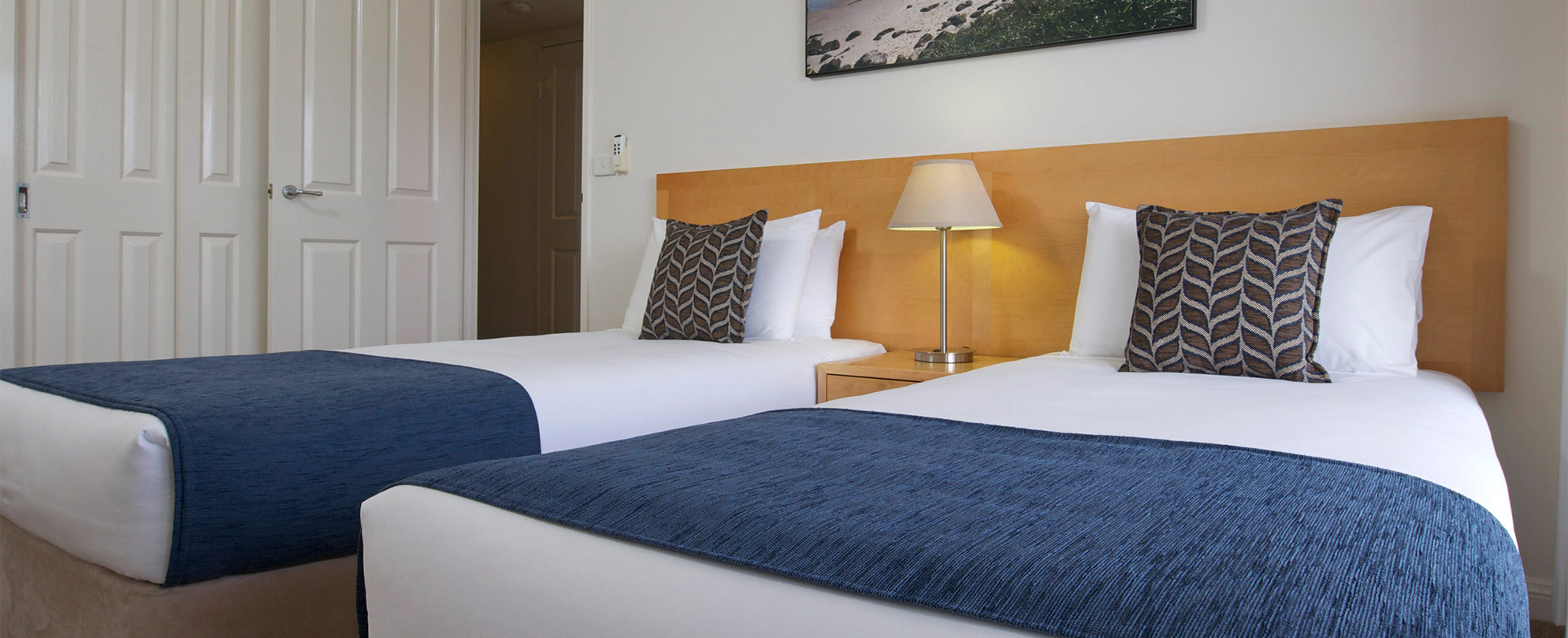 Two beds separated by a nightstand and lamp in a suite at Club Wyndham Port Macquarie.