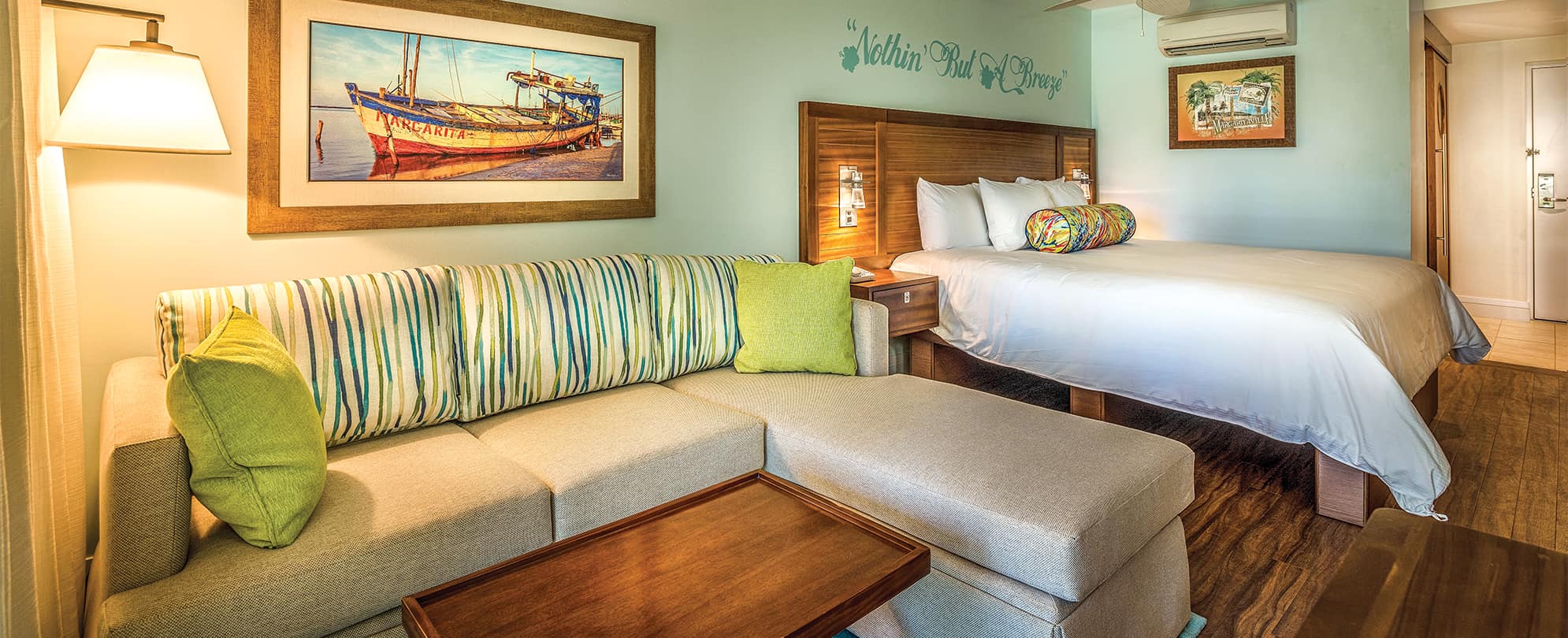 Tan sectional and bed with white linens in a studio suite at Margaritaville Vacation Club by Wyndham - St. Thomas.