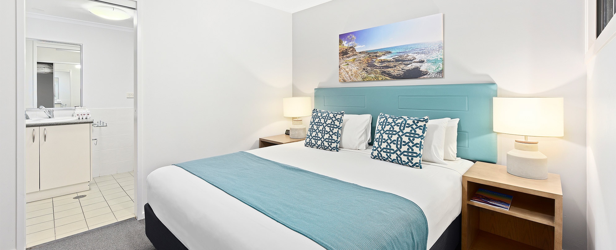 A bedroom with a king bed and 2 nightstands and lamps, and a connected bathroom in a Club Wyndham Flynns Beach ADA suite.