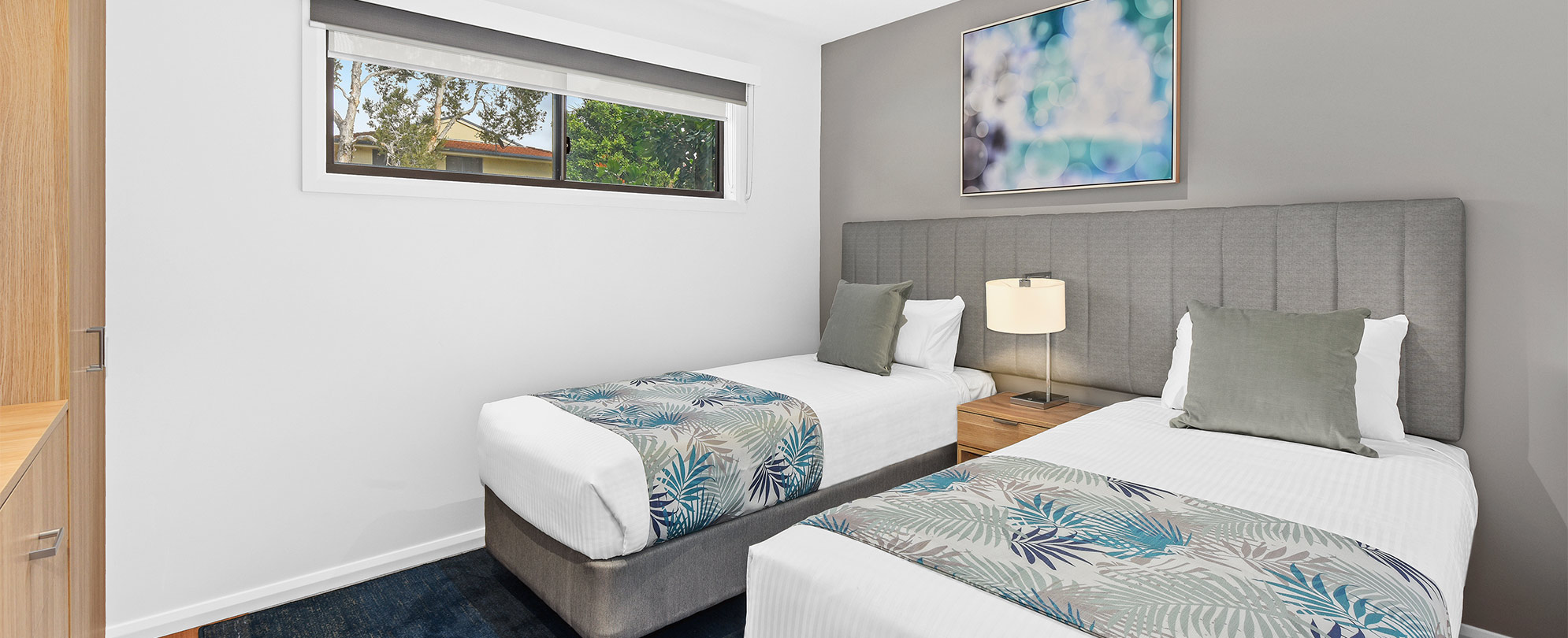 Two single beds with a nightstand and lamp in the bedroom of a Club Wyndham Flynns Beach deluxe suite. 