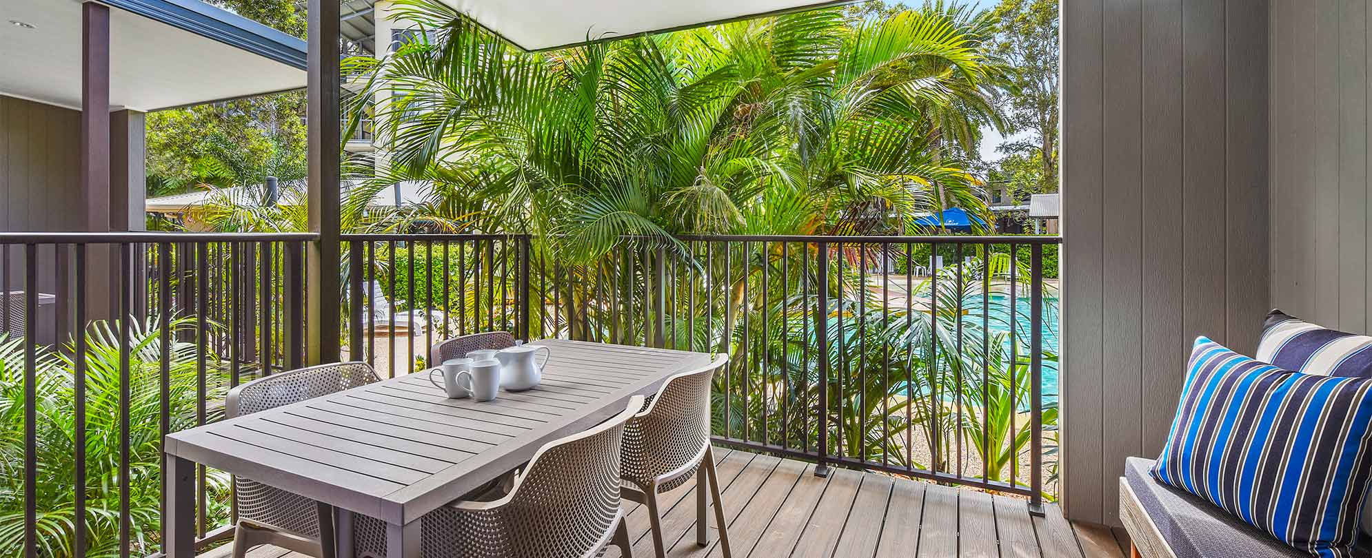 The balcony of a Club Wyndham Flynns Beach deluxe suite, with a table and 4 chairs overlooking the pool and palm trees.