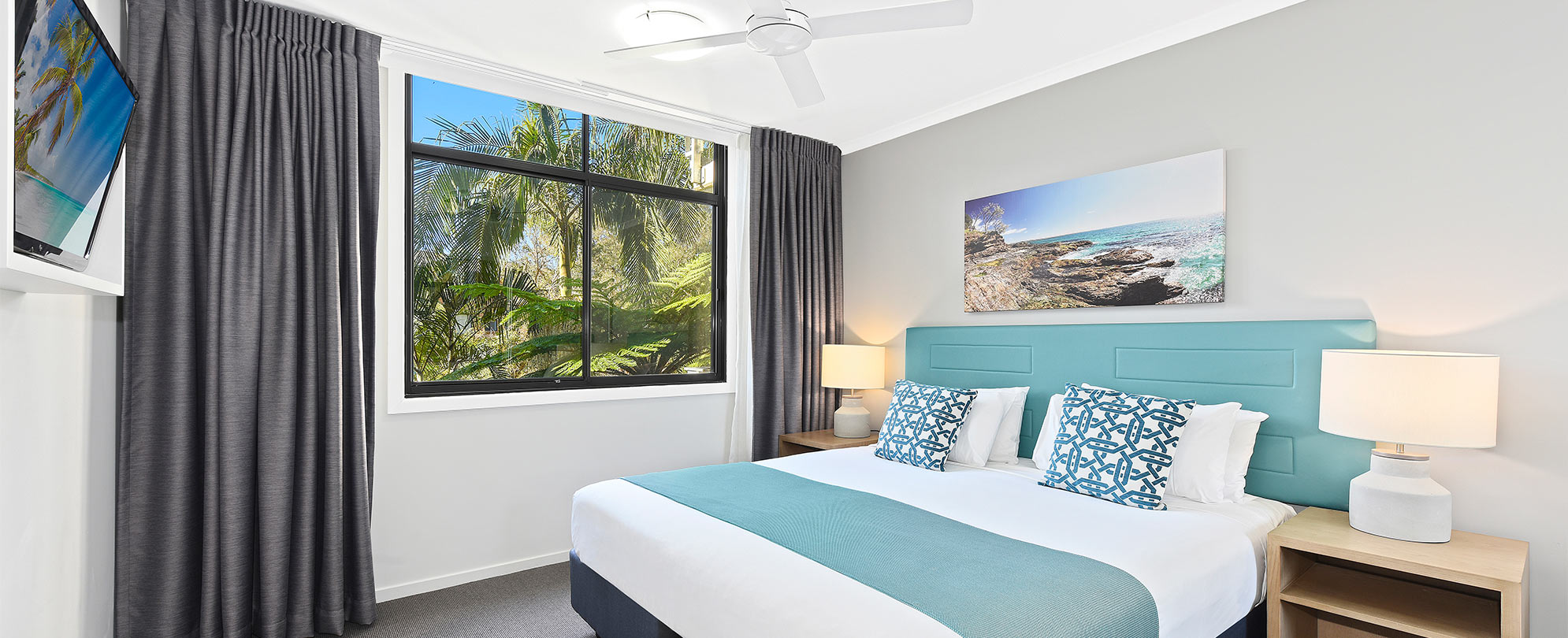 A king bed, 2 side tables with lamps, flat screen TV, and large window in a Club Wyndham Flynns Beach standard suite.