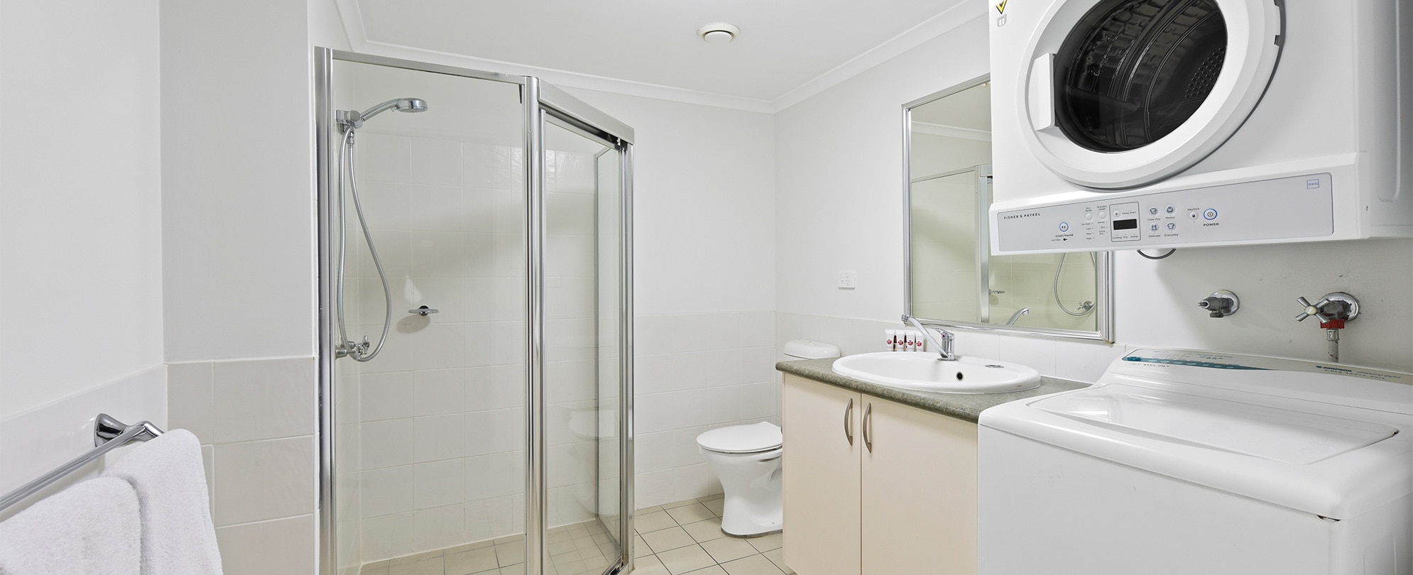 A bathroom with a shower, toilet, vanity, and washing and drying machine in a Club Wyndham Flynns Beach standard suite.