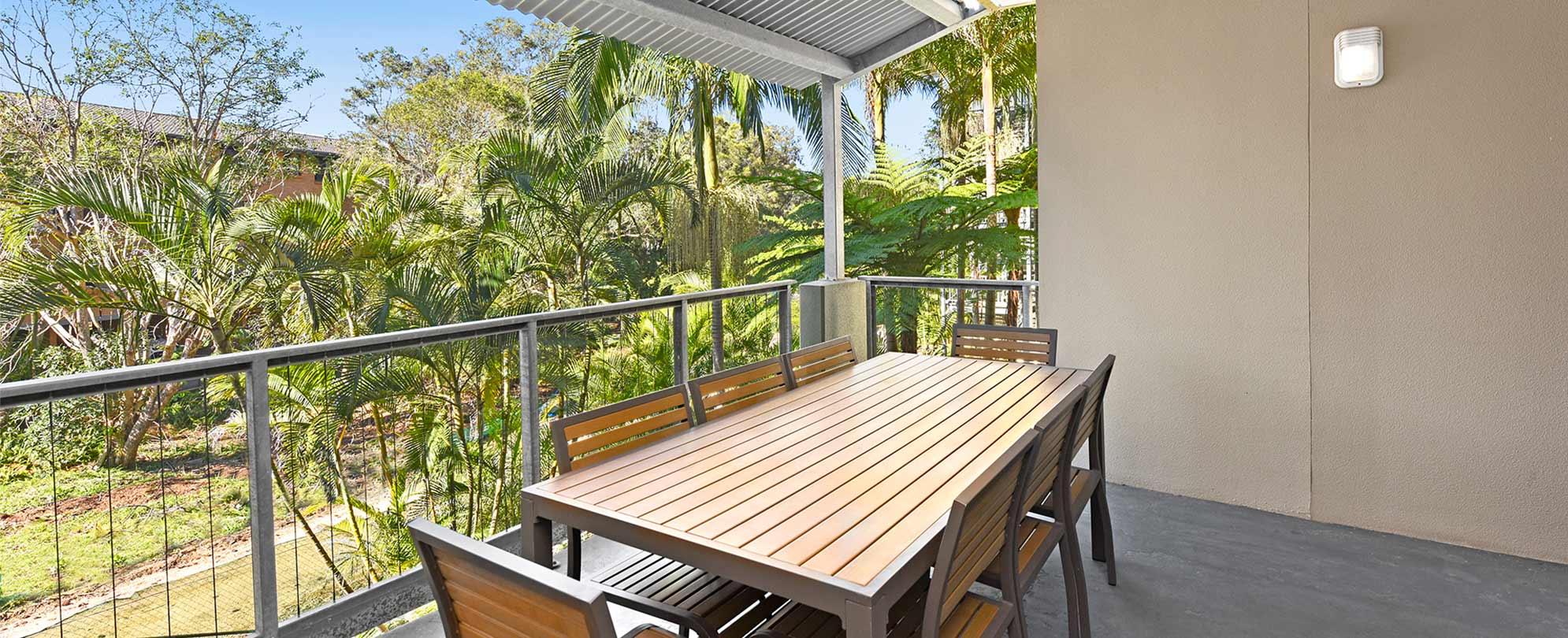 The balcony of a Club Wyndham Flynns Beach standard suite with a table and 8 chairs, with views of palm trees.