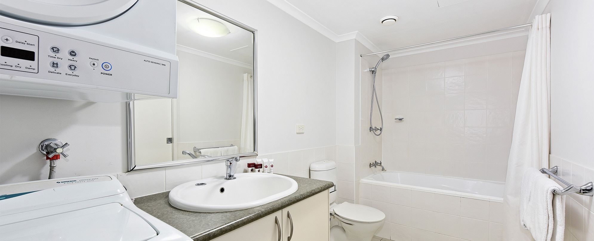 A bathroom with a shower/tub combo, toilet, vanity, and washer/dryer in a Club Wyndham Flynns Beach standard suite.