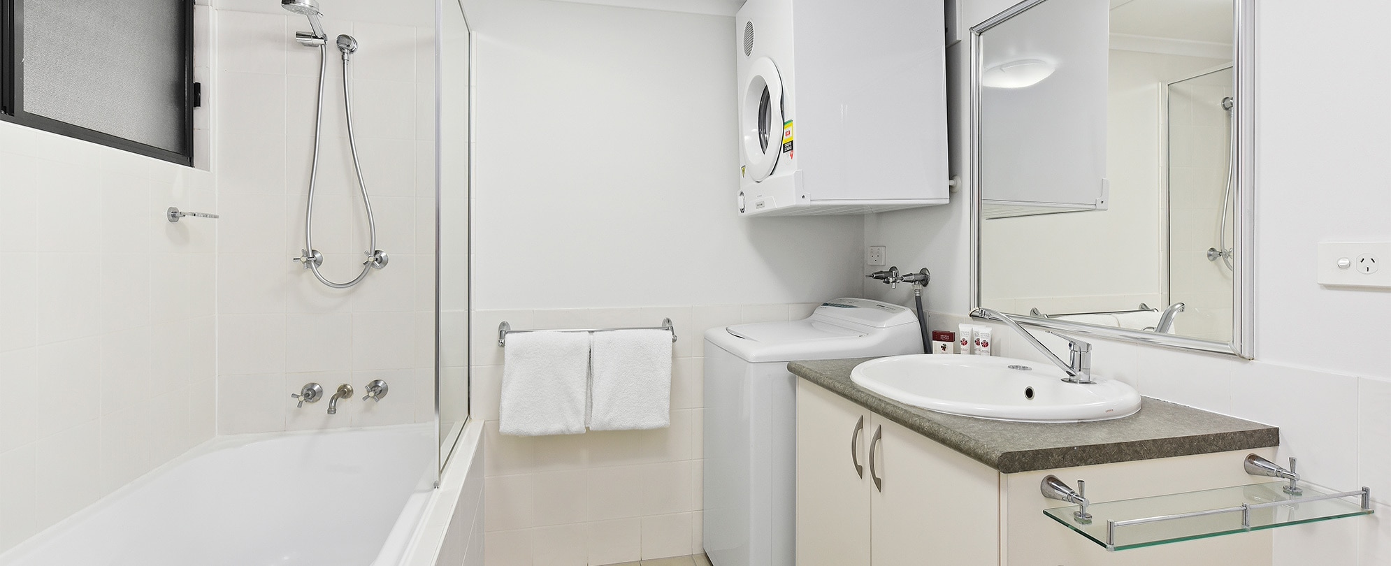 A bathroom with a shower/tub combo, toilet, vanity, and washer/dryer in a Club Wyndham Flynns Beach studio suite.
