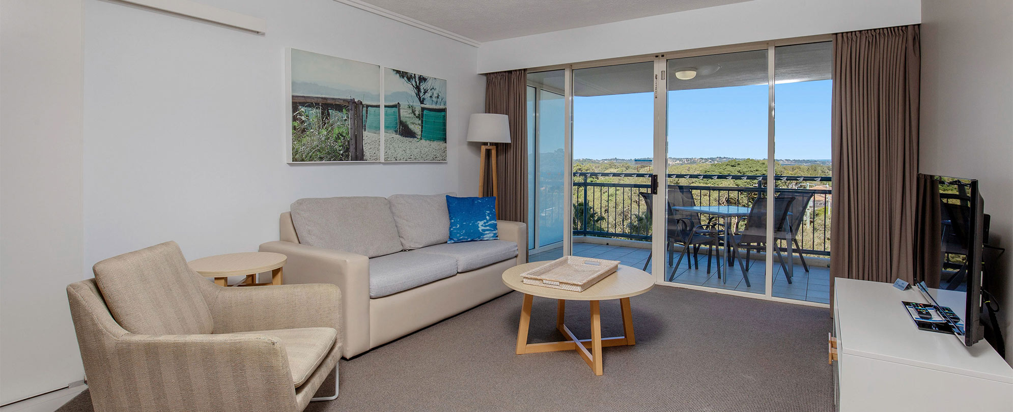 The living area of a Club Wyndham Kirra Beach ADA suite, with a couch, chair, flat screen tv, and sliding door to a balcony.