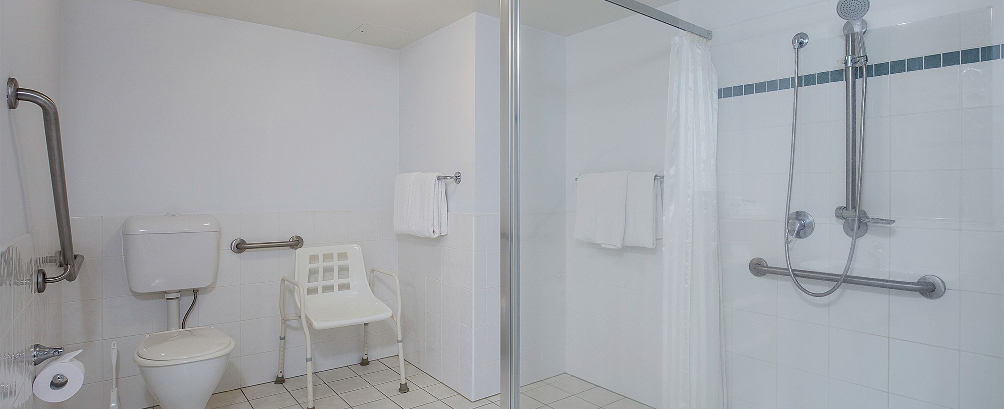 A shower, toilet, and a shower chair in the bathroom of a Club Wyndham Kirra Beach handicap accessible suite. 