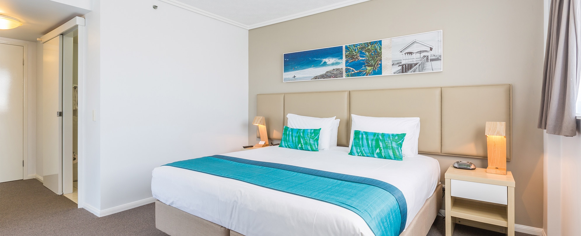A bedroom with a king bed with a headboard, and 2 nightstands with lamps in a Club Wyndham Kirra Beach standard suite.