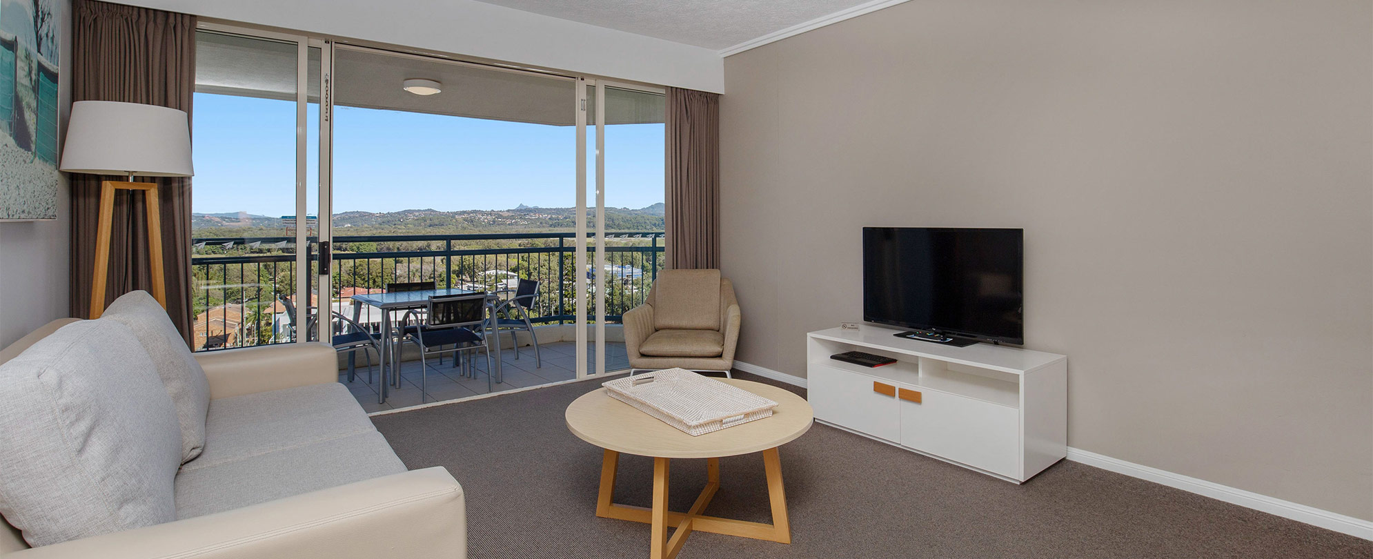 Couch, chairs, coffee table, flat screen TV, and sliding glass door to a patio in a Club Wyndham Kirra Beach standard suite.