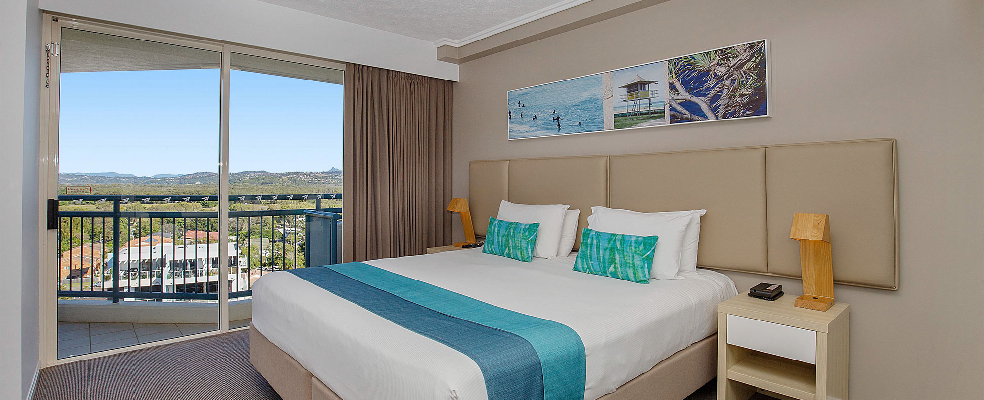 The bedroom of a Club Wyndham Kirra Beach standard suite with a king bed and sliding glass door leading to a balcony.