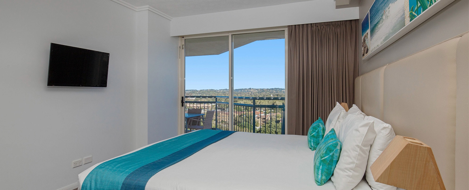 A bedroom with a king bed, flat screen tv, and sliding glass door to a balcony in a Club Wyndham Kirra Beach standard suite.