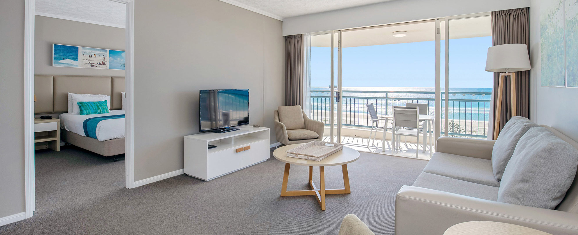 The living area of a Club Wyndham Kirra Beach ocean view suite with a couch, coffee table, tv and an open door to a bedroom.