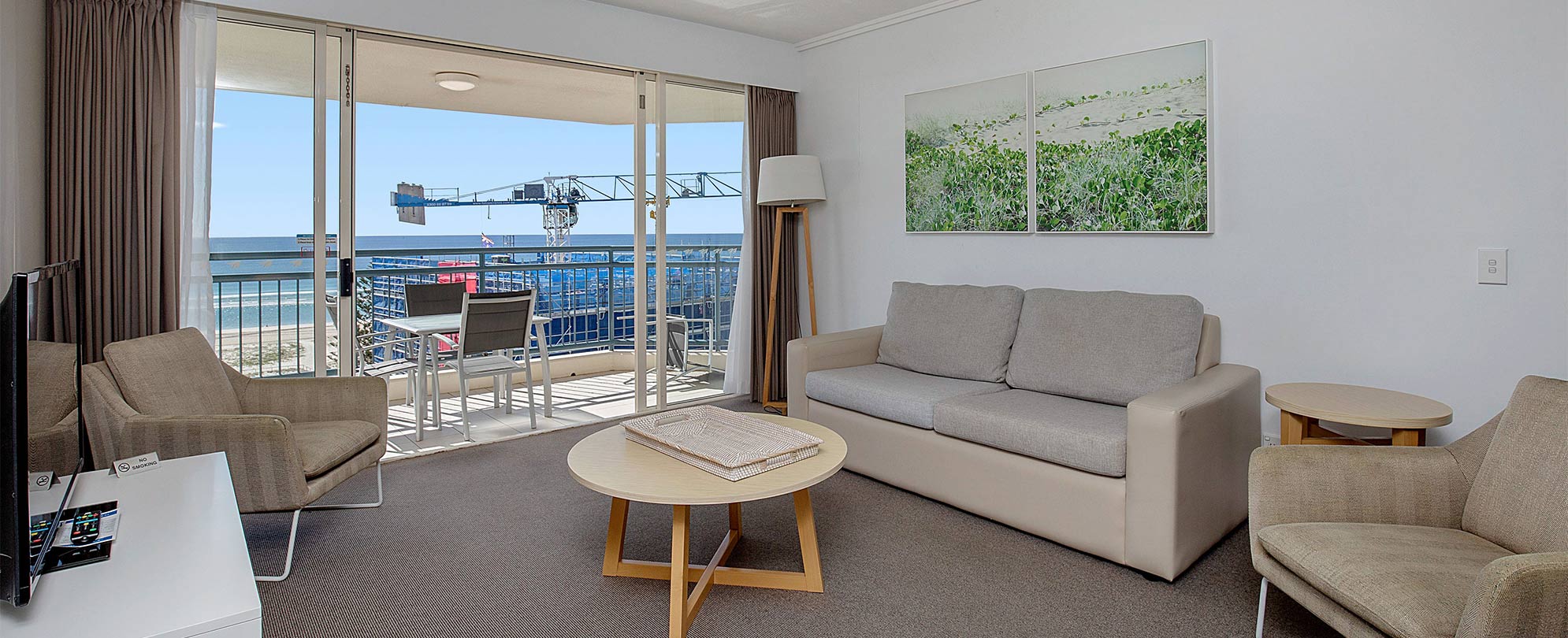 The living area of a Club Wyndham Kirra Beach ocean view suite with a couch, chairs, tv, and glass sliding door to a balcony.