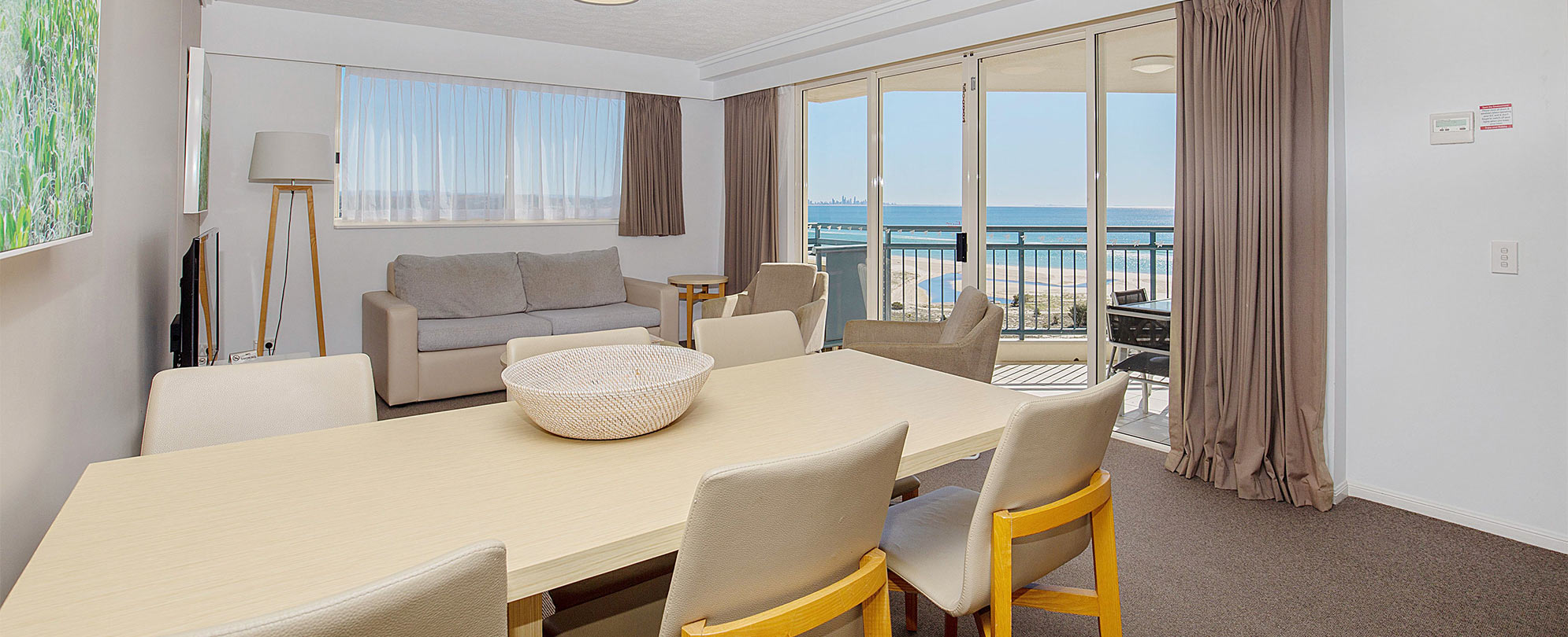 The dining table and living area of a Club Wyndham Kirra Beach ocean view suite with a sliding glass door to a balcony.