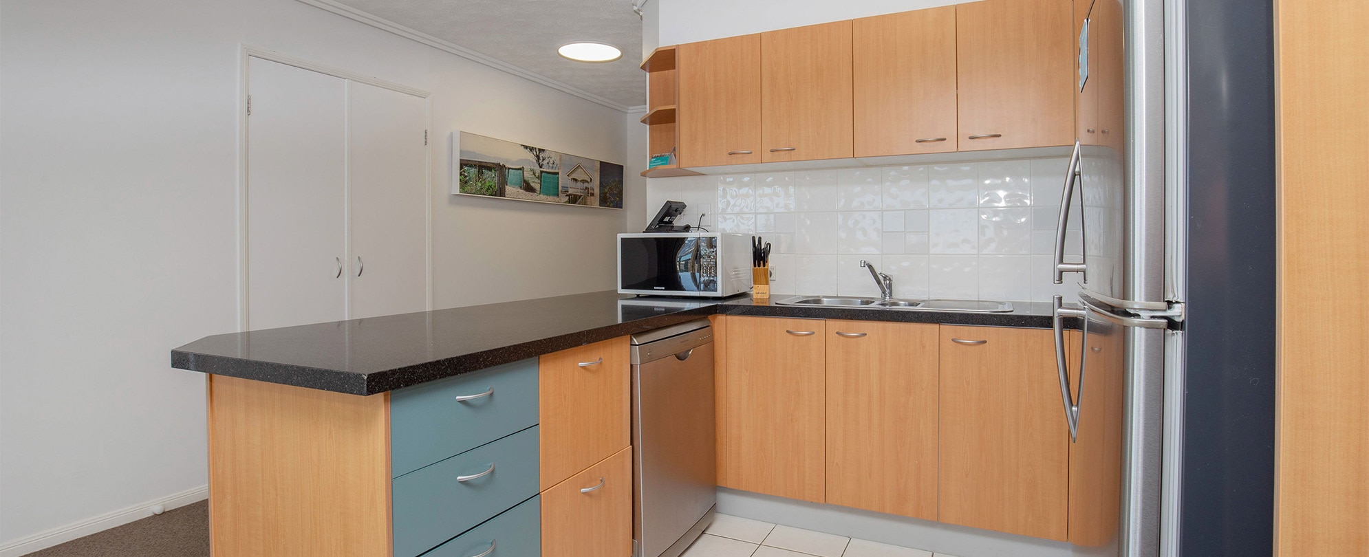 The kitchen of a Club Wyndham Kirra Beach standard suite with cabinets, a full fridge, microwave, sink, and dishwasher.
