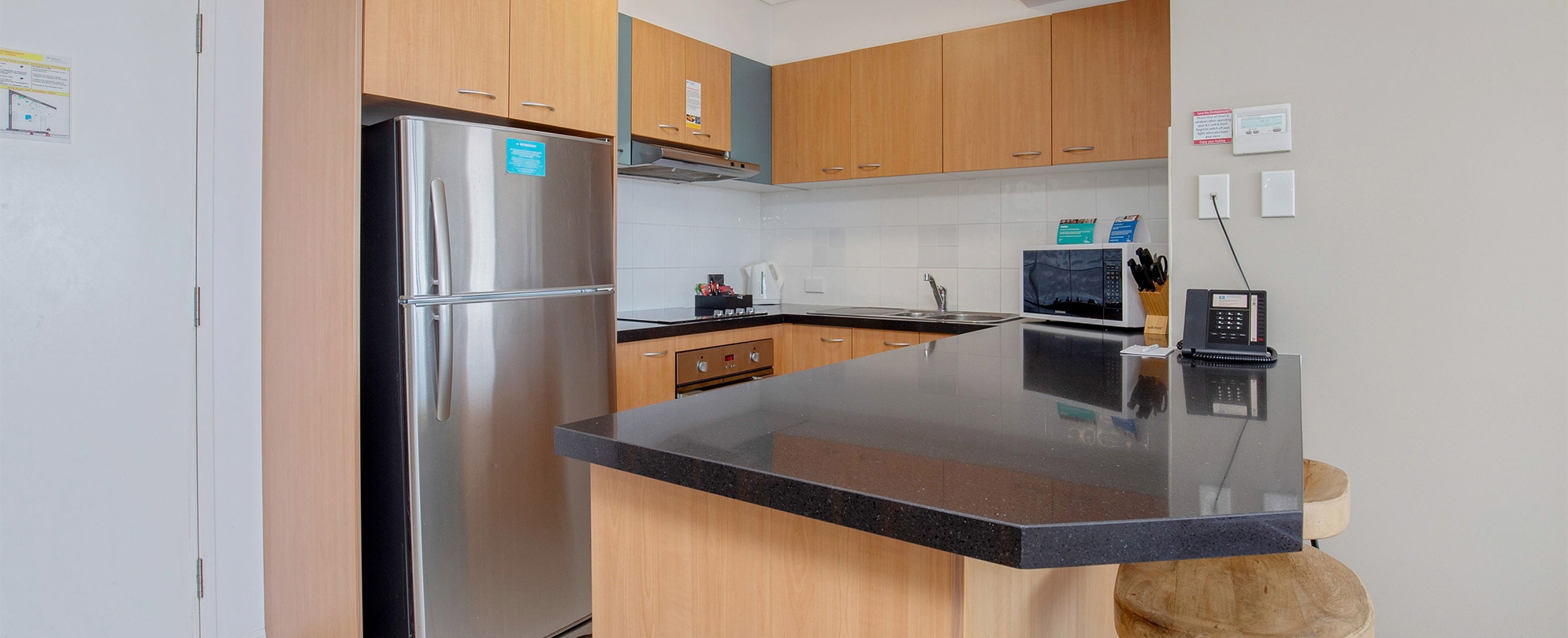 The kitchen of a Club Wyndham Kirra Beach standard suite with a full fridge, microwave, stove, countertop bar, and sink.