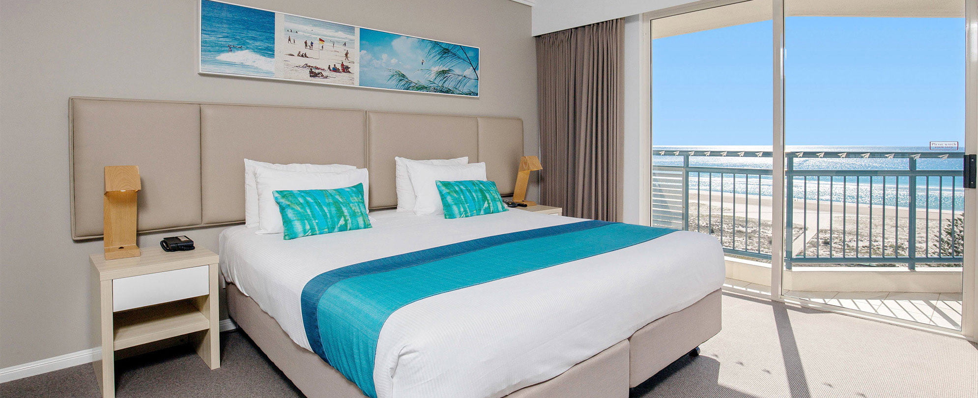 A bedroom with a king bed and sliding glass door leading to a balcony in a Club Wyndham Kirra Beach ocean view suite.