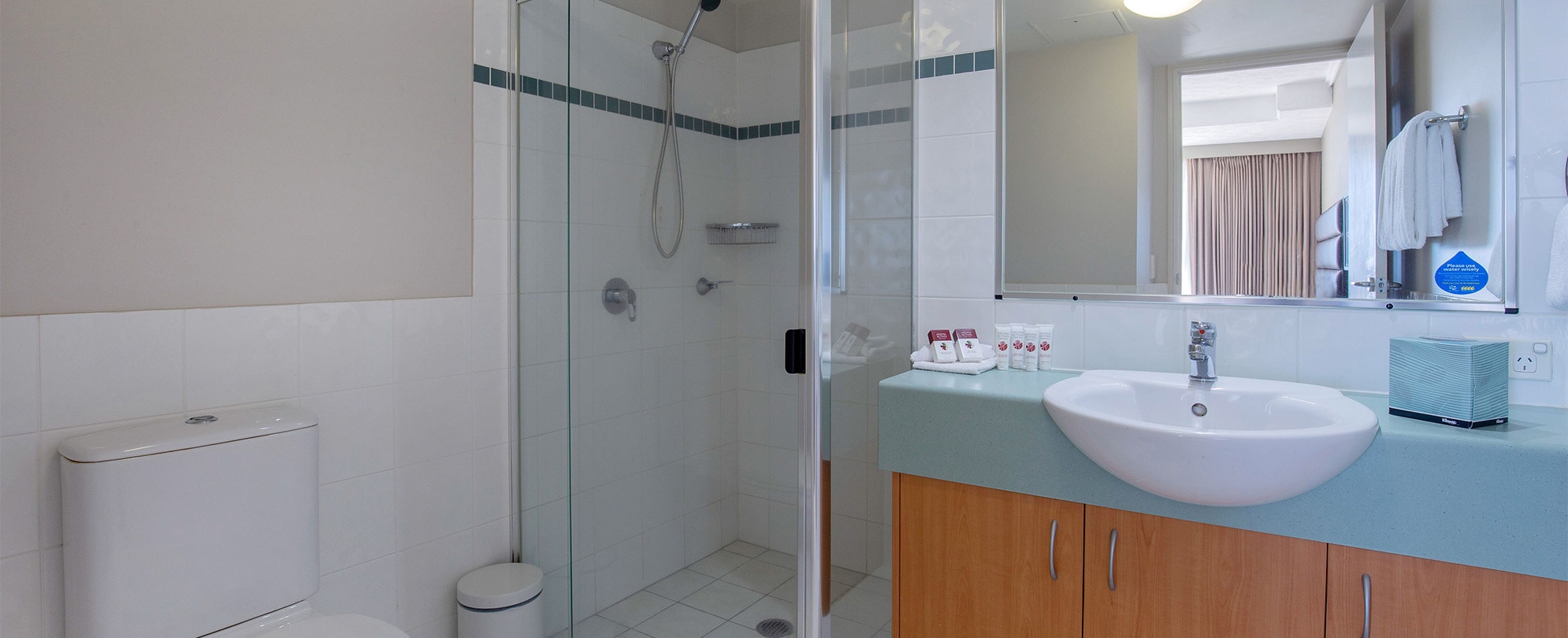 A bathroom with a shower, toilet, vanity sink, and mirror in a Club Wyndham Kirra Beach Standard Suite.