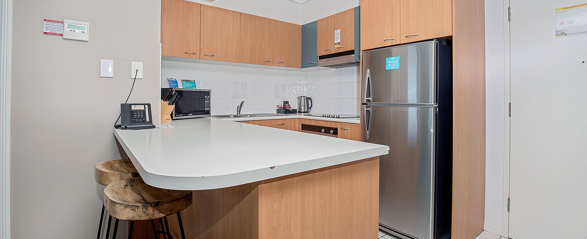 The kitchen of a Club Wyndham Kirra Beach standard suite with a full fridge, cabinets, a microwave, and 2 bar stools. 