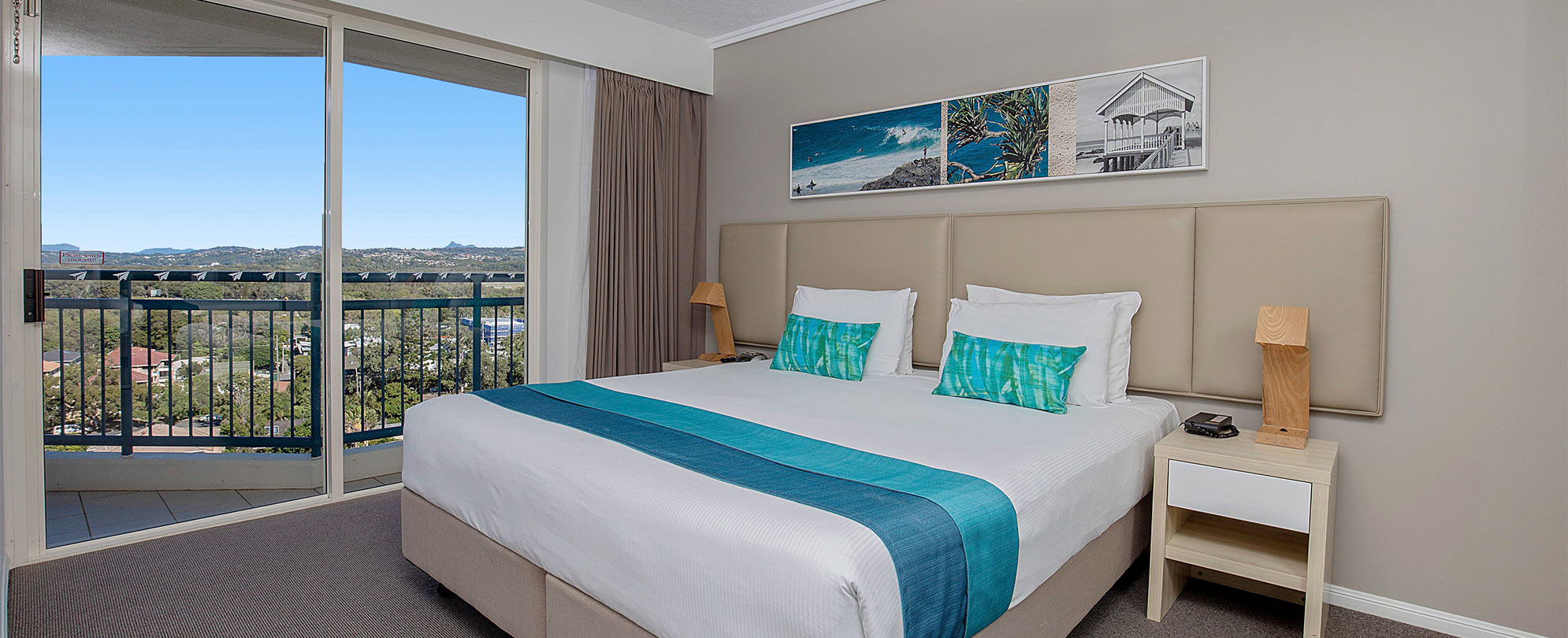 A bedroom with a king bed, 2 nightstands, and a sliding glass door to a balcony in a Club Wyndham Kirra Beach standard suite.