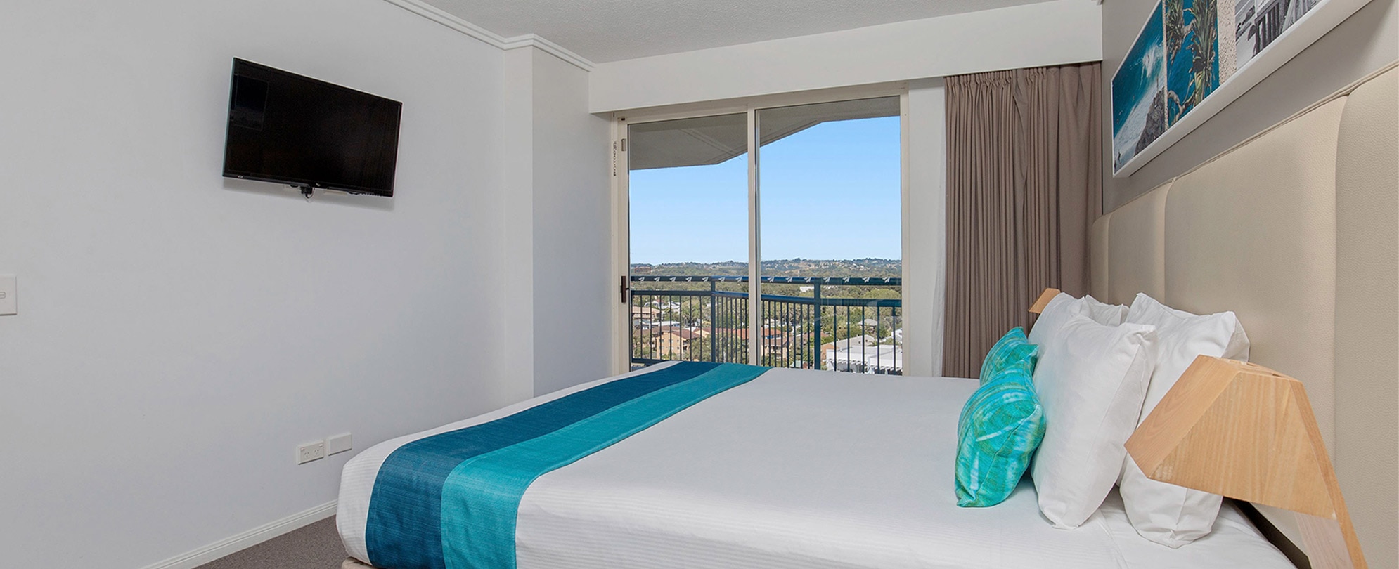 A bedroom with a king bed, flat screen tv, and a sliding glass door in a Club Wyndham Kirra Beach standard suite.