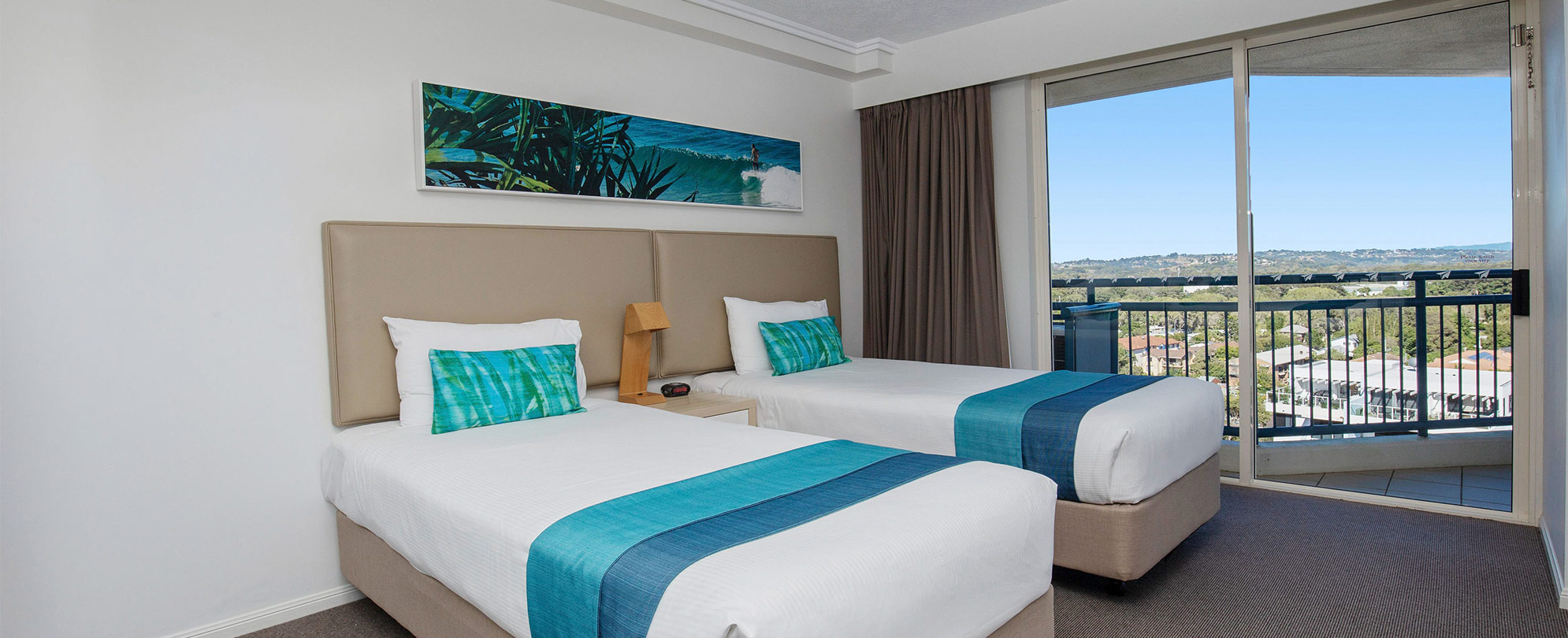 A bedroom two twin beds and a sliding glass door leading to a balcony in a Club Wyndham Kirra Beach standard suite.
