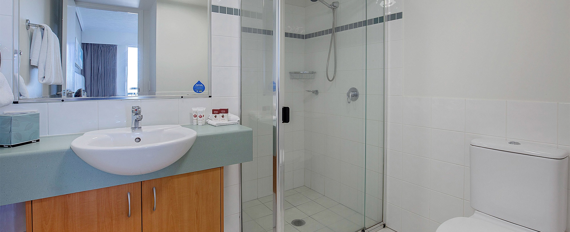 A bathroom with a shower, toilet, vanity sink, and mirror in a Club Wyndham Kirra Beach Standard Suite.