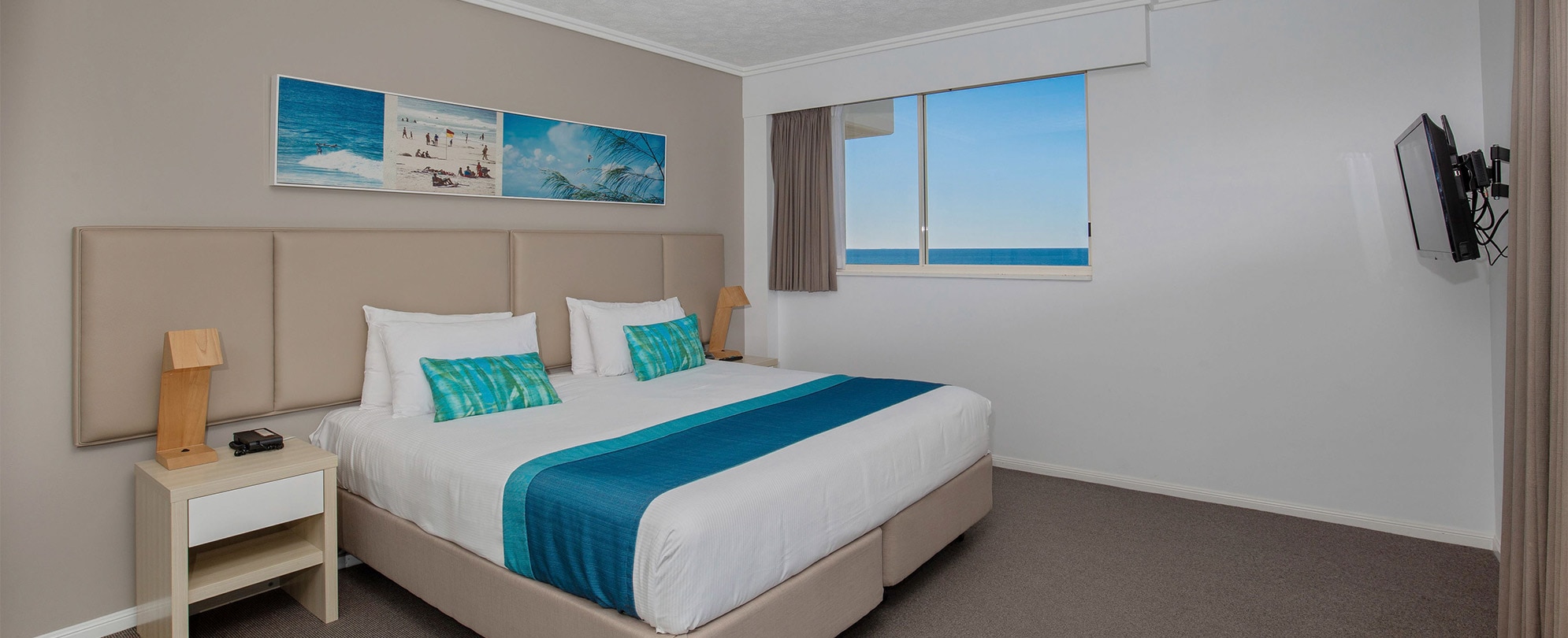 A bedroom with a king bed, two nightstands, and a flat screen tv in a Club Wyndham Kirra Beach standard suite.