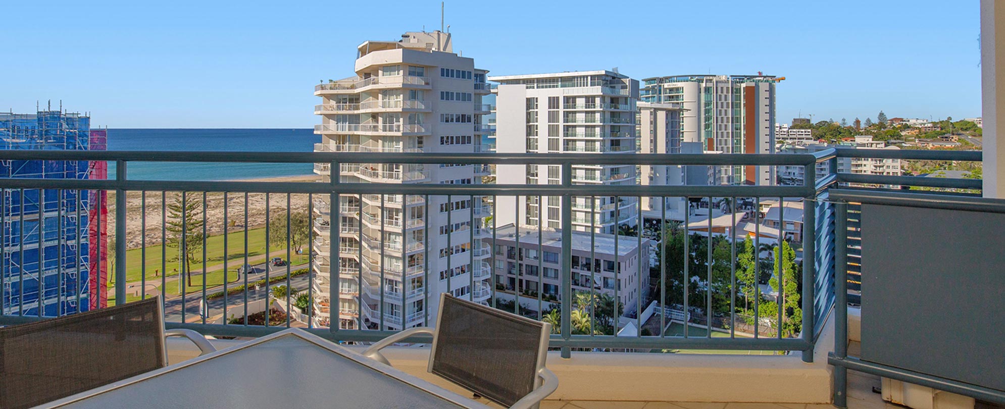 A balcony with a table and 4 chairs of a Club Wyndham Kirra Beach standard suite with a view of the ocean and high rises.